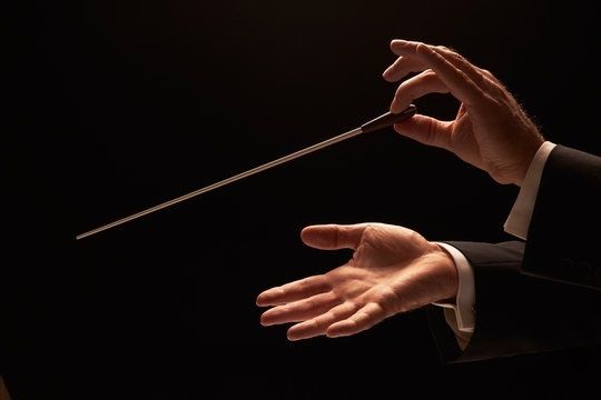 Hände eines Dirigenten mit Taktstock vor schwarzem Hintergrund